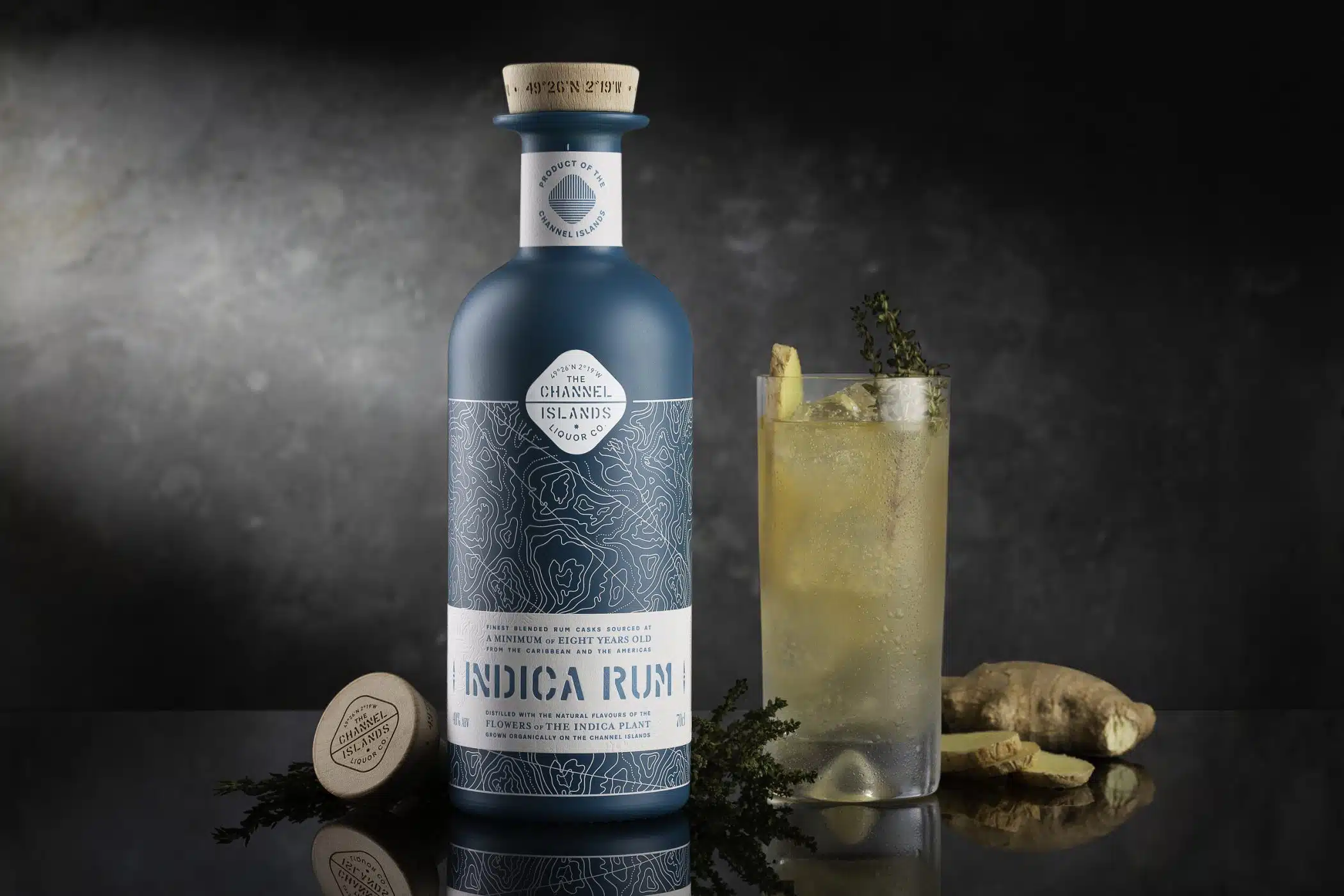 A blue bottle of Indica Rum with a glass and a grey background