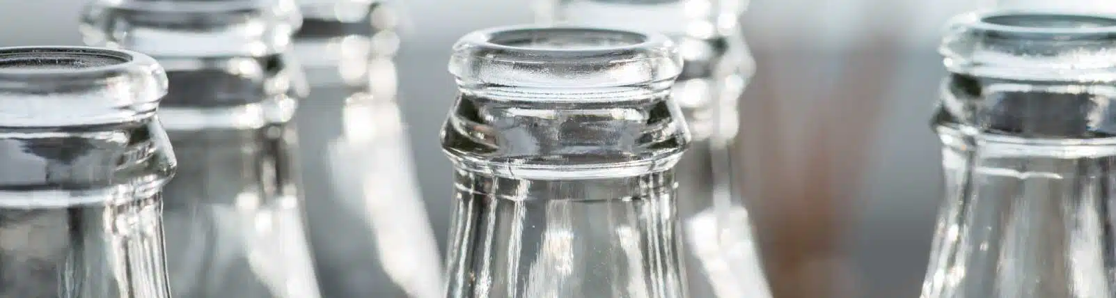 A close-up of the tops of clear glass bottles, focusing on the bottle rims and necks