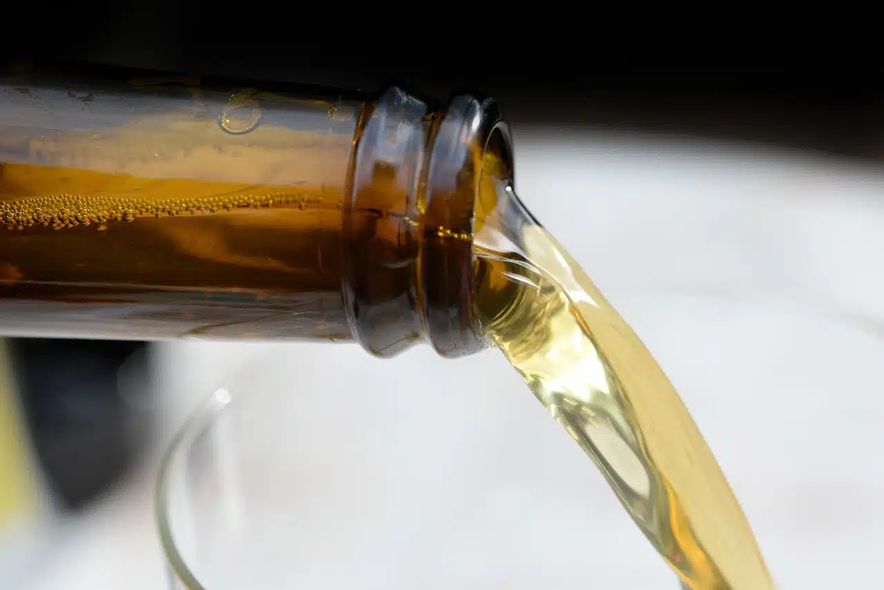 Close-up of a golden beverage being poured from a brown glass bottle into a glass, with bubbles visible inside the bottle.