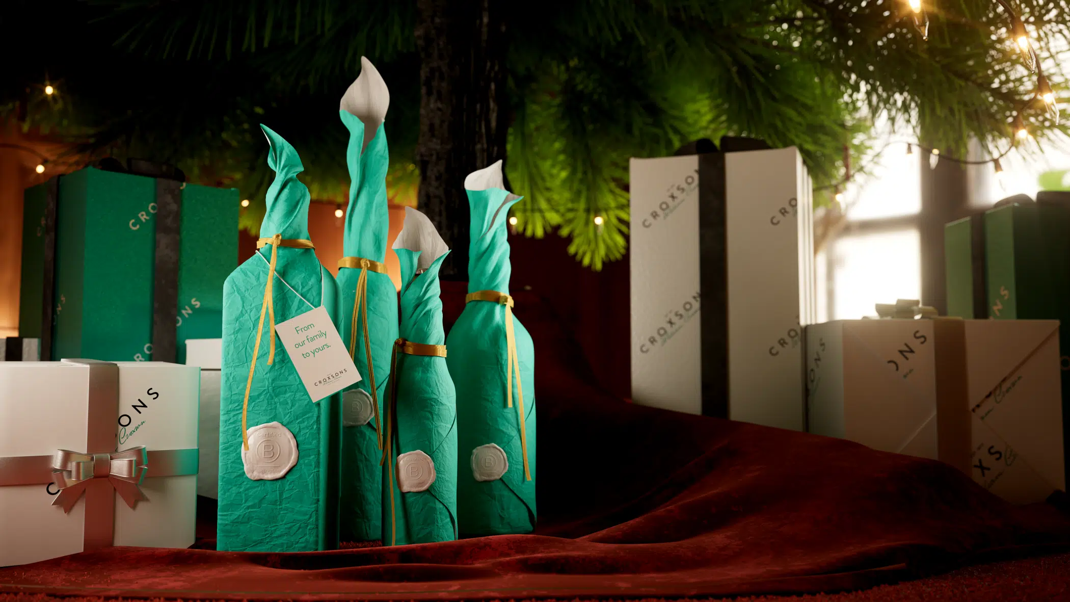 "Festive scene featuring Croxsons gift boxes and bottles wrapped in teal tissue with wax seals and tags reading ‘From our family to yours,’ displayed under a Christmas tree with warm lights.