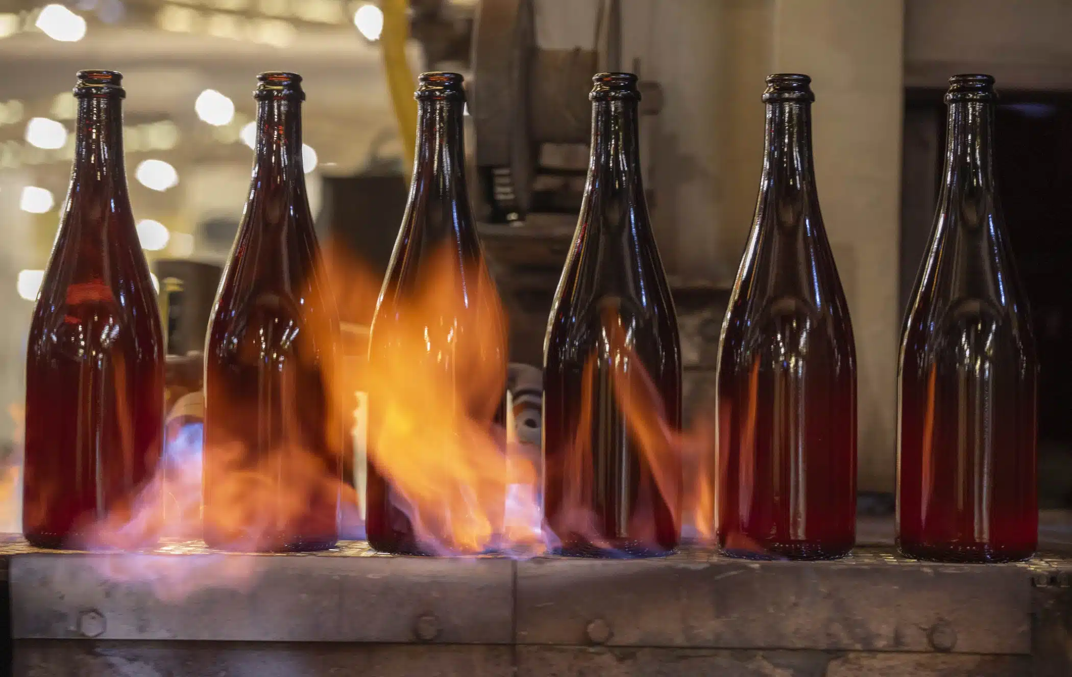 Amber sparkling wine bottle, sovereign, on a production line with flames.