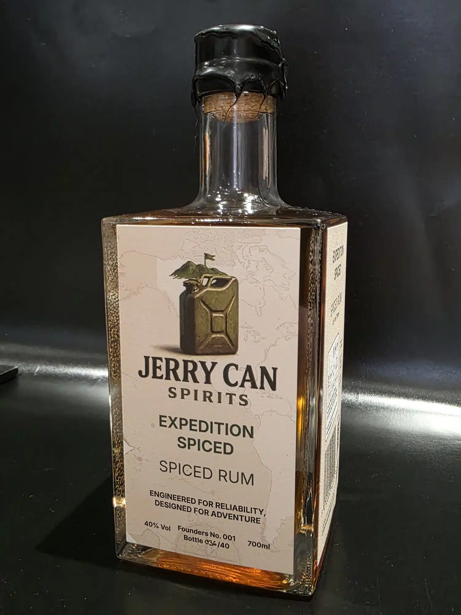 Front view of a square glass bottle of Jerry Can Spirits Expedition Spiced Rum, filled with amber-coloured rum and sealed with a natural cork finished in hand-dipped black wax.
